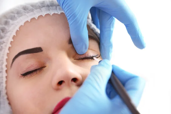 Cosmetologist applying permanent make up on eyes, close-up