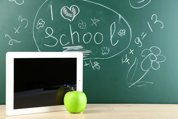 Digital tablet and apple on  desk in front of blackboard