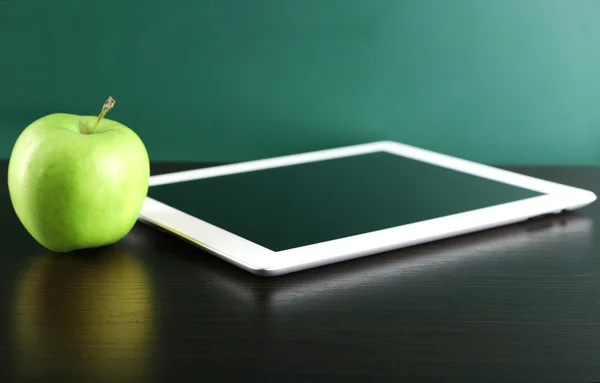 Digital tablet and apple on  desk in front of blackboard