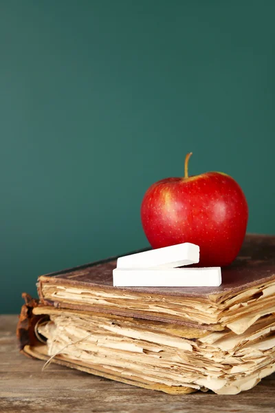 Old books, apple and chalk on blackboard background