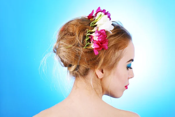 Portrait of young woman with flowers in hair on blue background