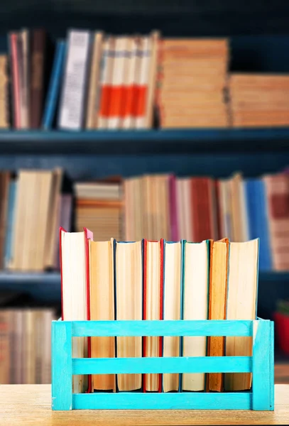 Books in wooden crate on bookshelves background