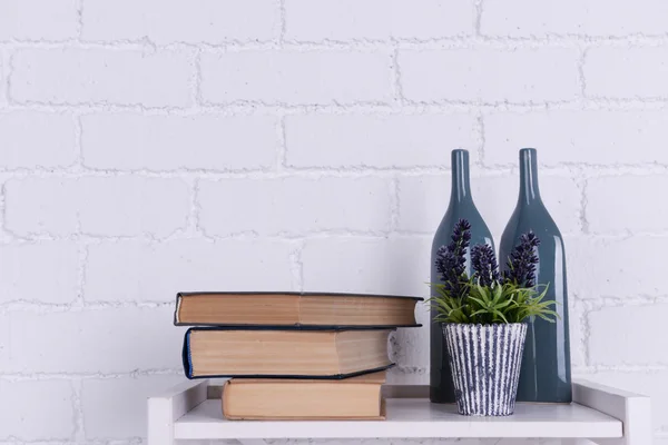 Interior design with plant, glass bottles and stack of books on tabletop on white brick wall background