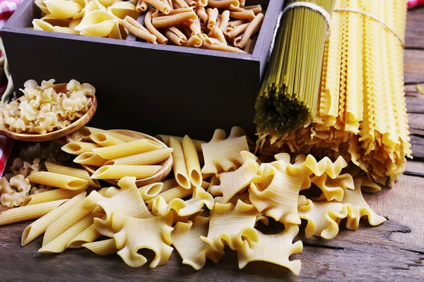 Different types of pasta in wooden box with napkin on wooden table background