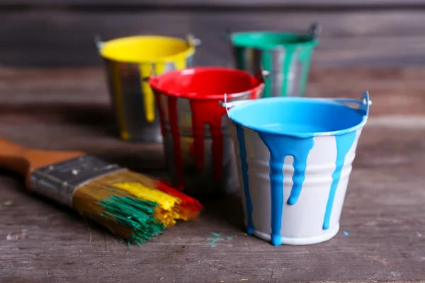 Metal buckets with colorful paint on wooden background