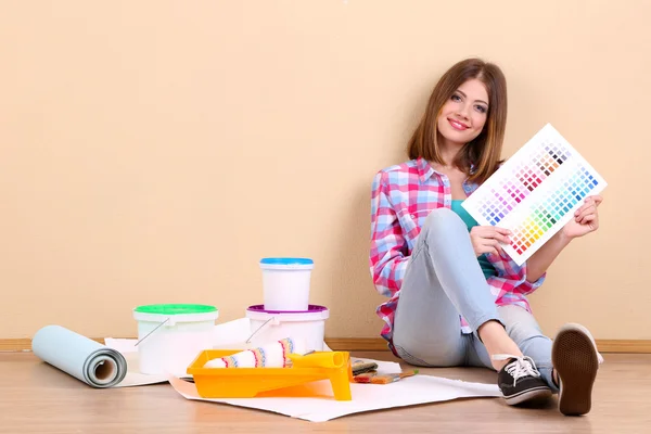 Beautiful girl sitting on floor with equipment for painting wall