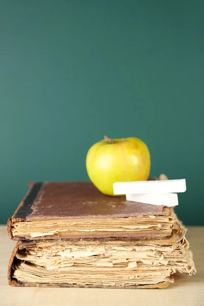 Old books, apple and chalk on blackboard background