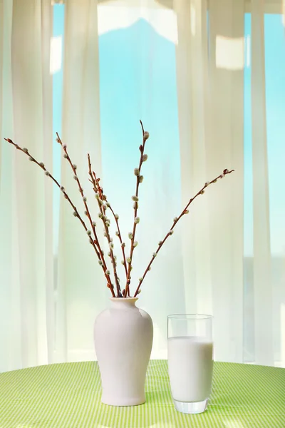 Willow twigs and glass of milk on table on curtains background