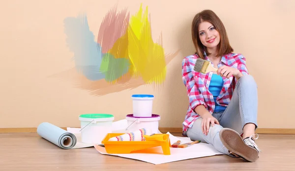 Beautiful girl sitting on floor with equipment for painting wall