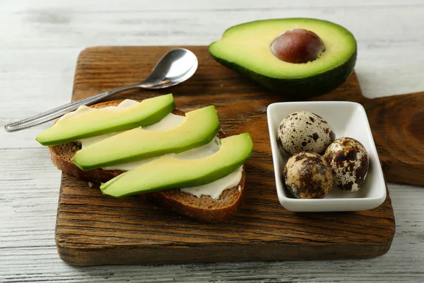 Slice of rye bread with sliced avocado and boiled quail eggson color wooden background