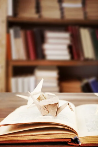 Open book with paper cranes on bookshelves background