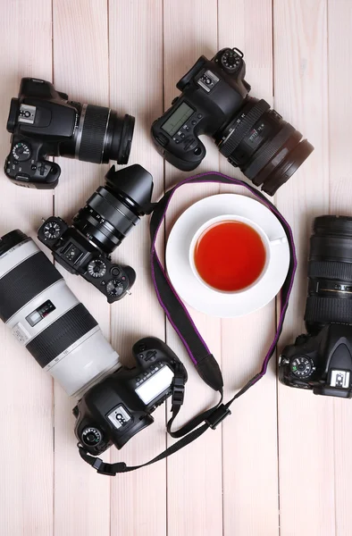 Modern cameras with cup of tea on wooden table, top view