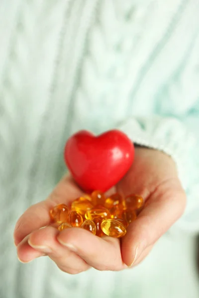 Hand holding red heart and cod liver oil, close up