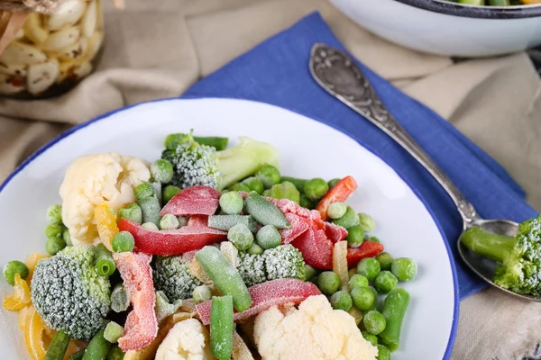 Frozen vegetables on plate on napkin, on wooden table background