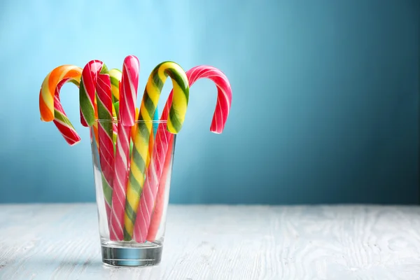 Colorful candy canes in glass on table on blue background