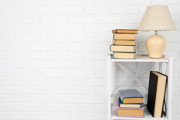 Wooden shelf with books and lamp on brick wall background