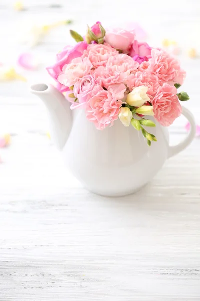 Beautiful spring flowers in teapot on wooden table, closeup