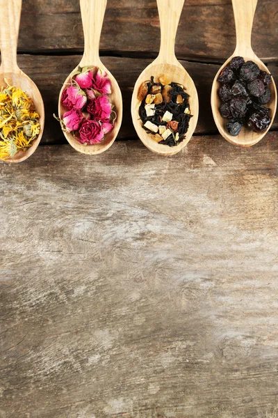 Collection of tea and natural additives in wooden spoons, on old wooden table