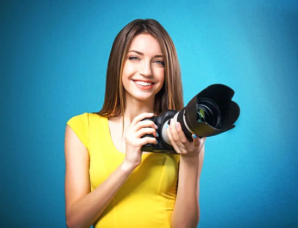 Young female photographer taking photos on blue background