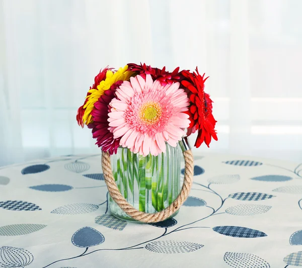 Glass vase of colorful gerbera flowers on table on curtains background