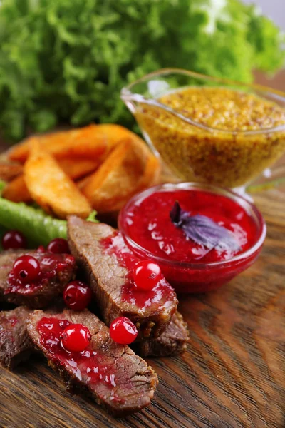 Beef with cranberry sauce, roasted potato slices on cutting board, on wooden background