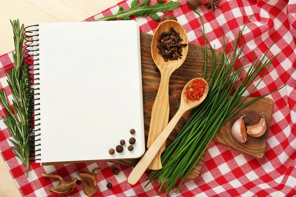 Open recipe book with fresh herbs and spices on wooden background