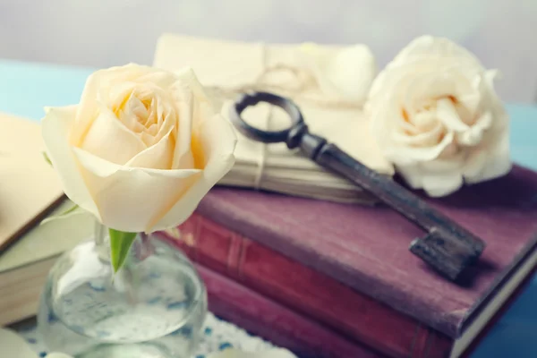 Fresh roses with old book and letters on color wooden table, on bright background. Vintage concept
