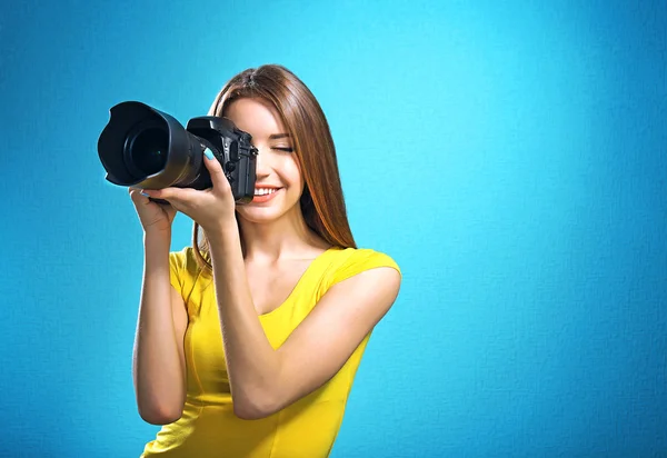 Young female photographer taking photos on blue background