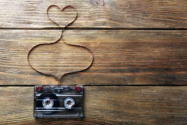 Audio cassette with magnetic tape in shape of heart on wooden background