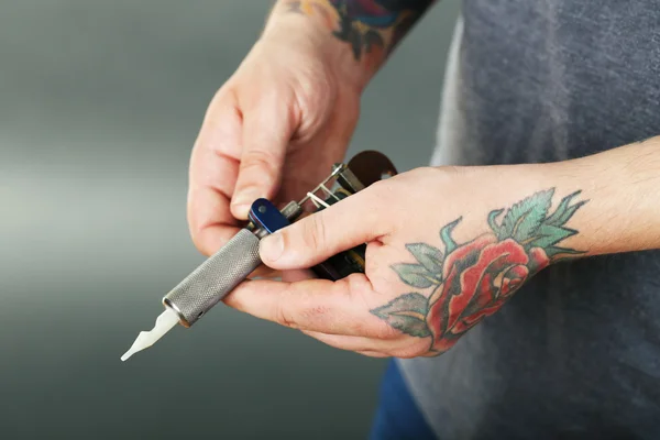 Hand of tattoo artist with tattoo machine, closeup