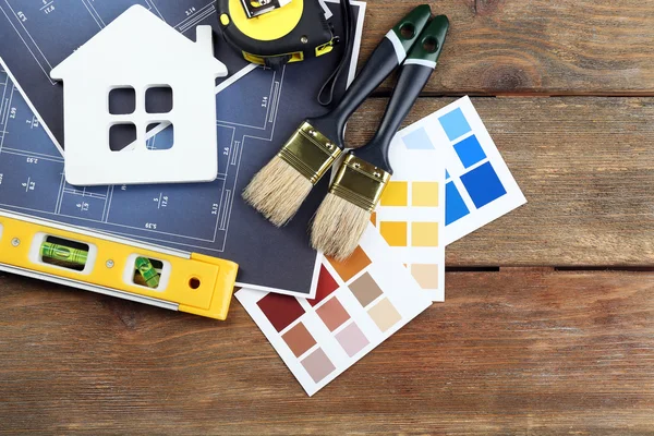 Color samples, decorative house, gloves and paintbrushes on wooden table background