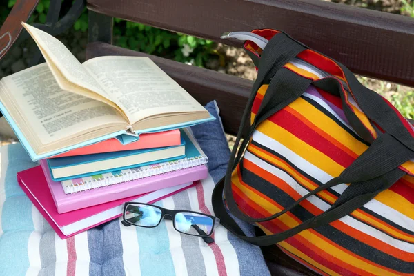 Books, glasses and bag on bench outdoors