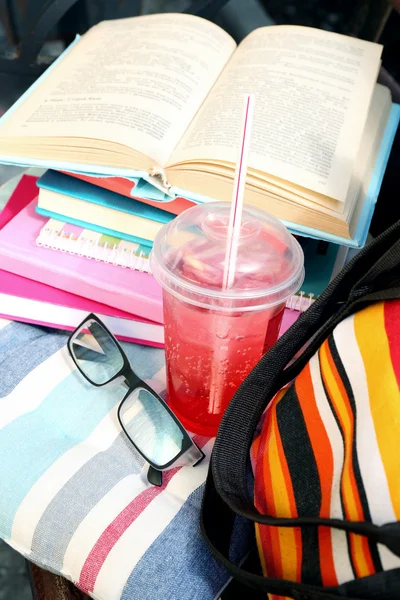 Books, glasses, drink and bag on bench outdoors