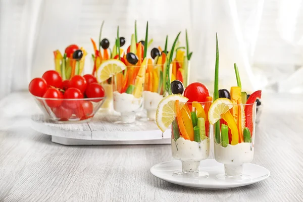 Snack of vegetables in glassware on wooden table on curtains background