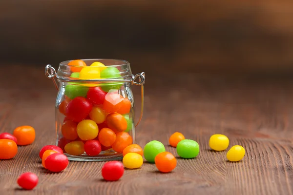 Colorful candies in jar on table on wooden background