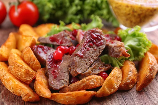 Beef with cranberry sauce, roasted potato slices and bun on wooden cutting board, close-up