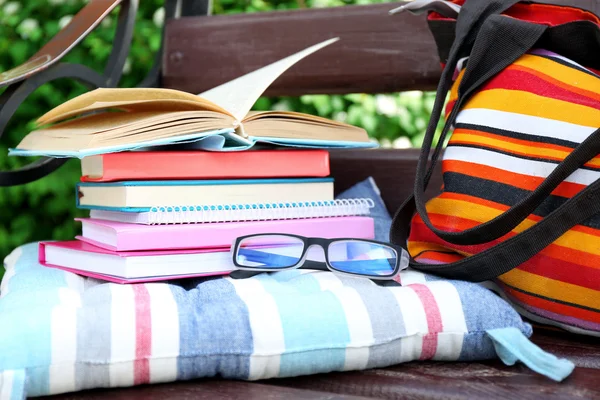 Books, glasses and bag on bench outdoors