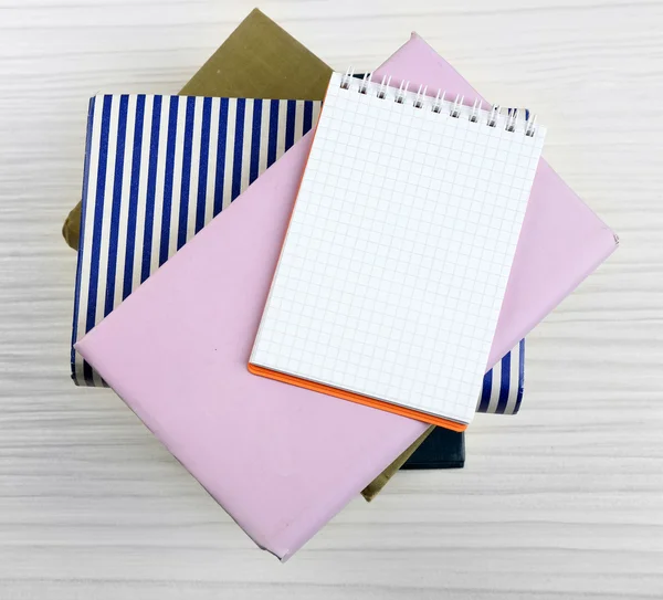 Notebook on top of pile of books and magazines on wooden background