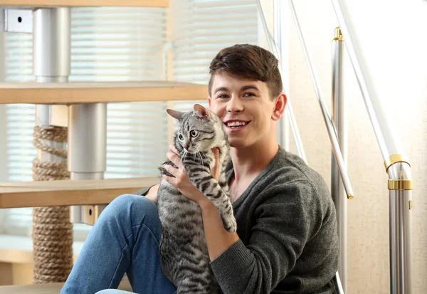 Handsome young man with cute cat sitting on steps at home