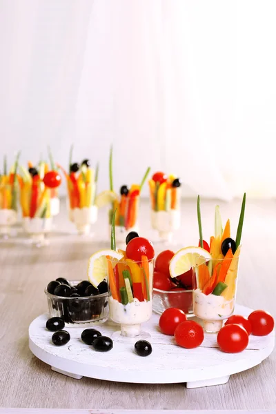 Snack of vegetables in glassware on wooden table on curtains background