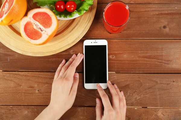 Food and mobile phone in female hands on wooden background