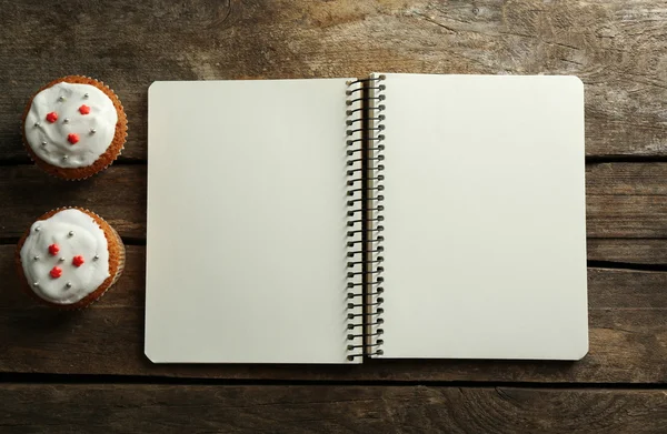 Open recipe book and tasty bakery on wooden background