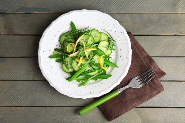 Green salad with cucumber, arugula and lemon peel on wooden table, top view