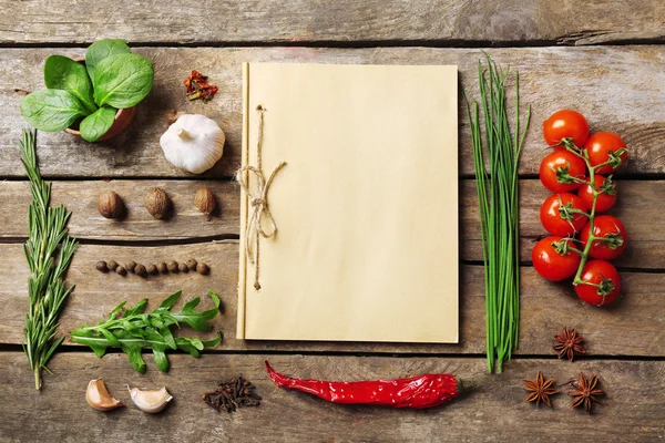 Open recipe book with fresh herbs, tomatoes and spices on wooden background