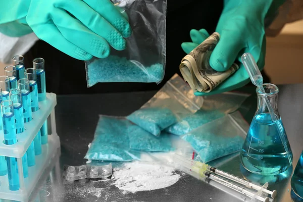 Chemists holding plastic bag with blue methamphetamine and money