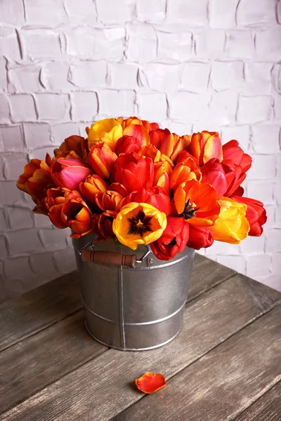 Beautiful bouquet of tulips in metal bucket on wall background