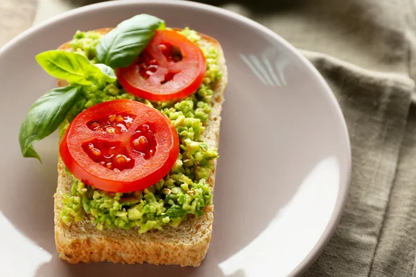 Vegan sandwich with avocado and vegetables on plate, on wooden background