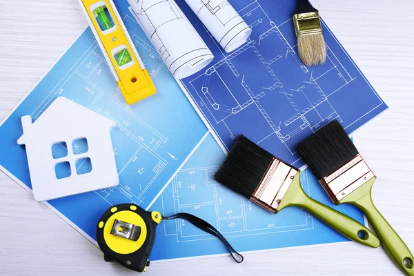 Construction instruments, plan and brushes over house plan on wooden table background