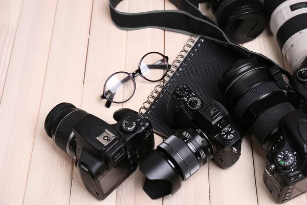 Modern cameras with glasses and notebook on wooden table, closeup