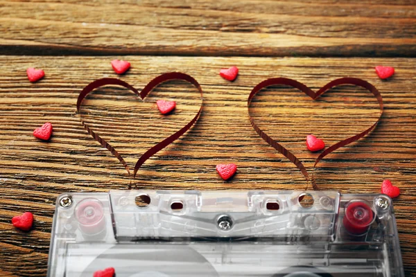 Audio cassette with magnetic tape in shape of hearts on wooden background